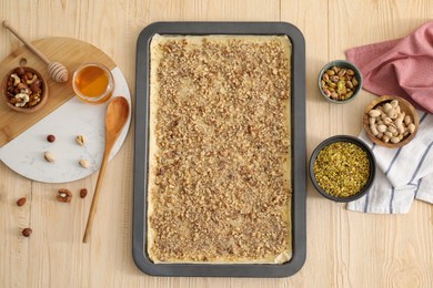 Photo of Making delicious baklava. Baking pan with dough and ingredients on wooden table, flat lay