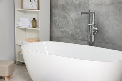 Stylish bathroom interior with ceramic tub, care products and towels in cabinet