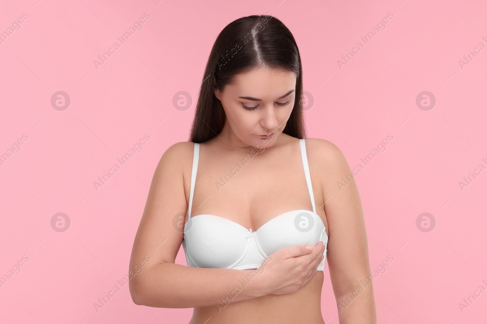 Photo of Mammology. Woman in bra doing breast self-examination on pink background