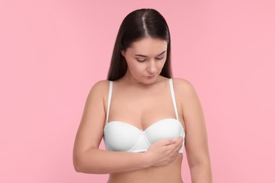 Mammology. Woman in bra doing breast self-examination on pink background