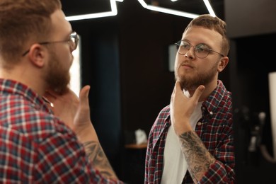 Young bearded man near mirror in barbershop