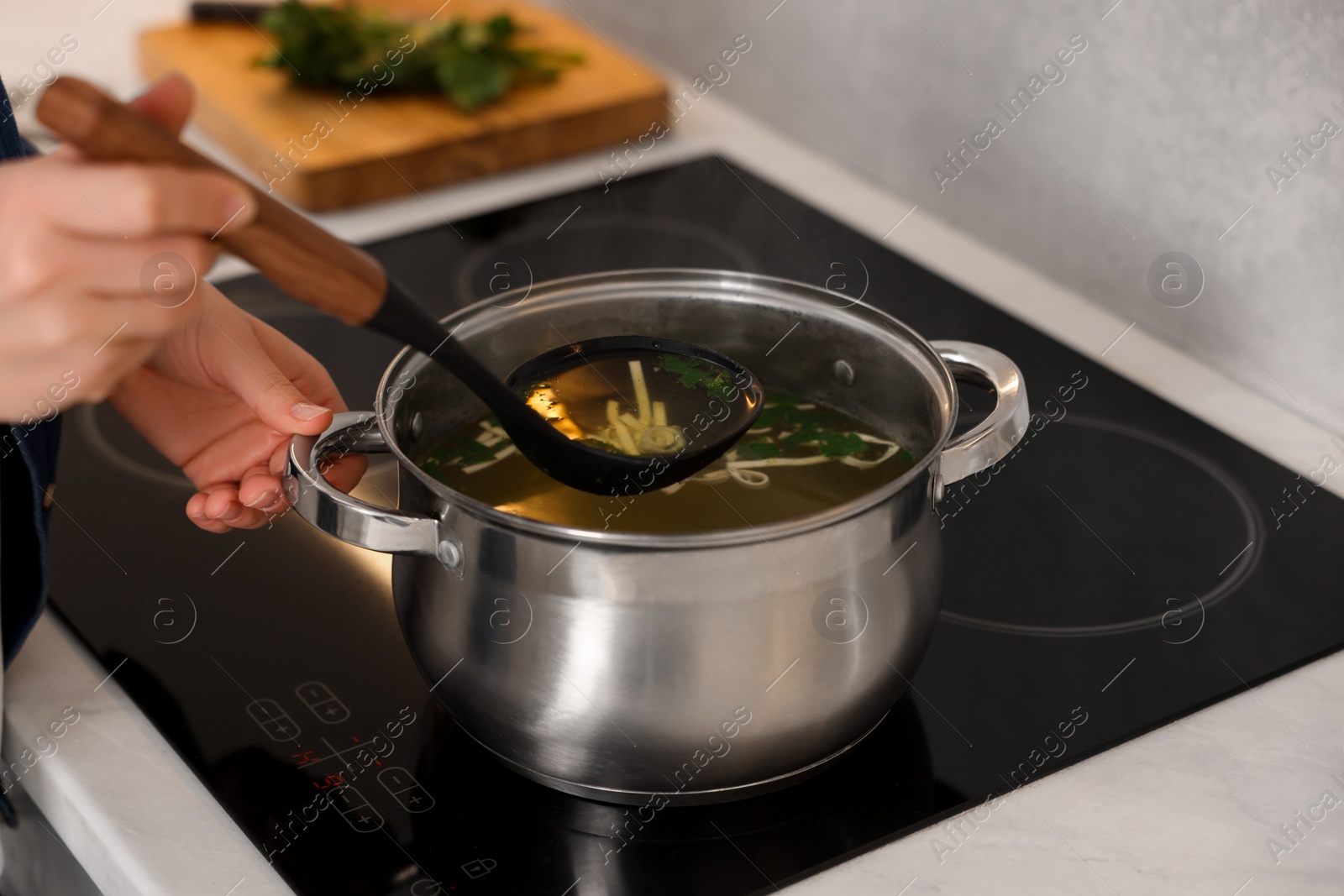 Photo of Woman cooking soup at countertop in kitchen, closeup