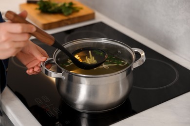 Woman cooking soup at countertop in kitchen, closeup