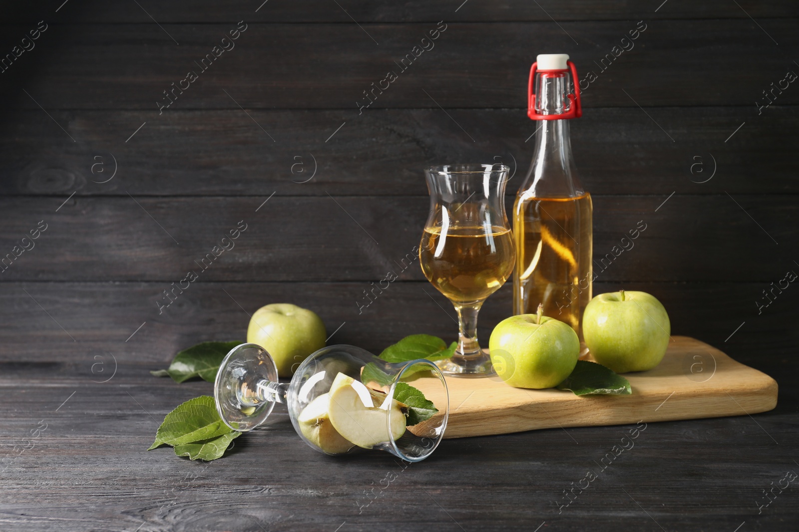 Photo of Delicious cider and apples with green leaves on black wooden table, space for text