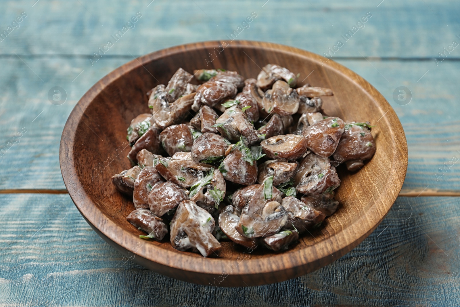 Photo of Bowl of fried mushrooms with sauce on wooden table