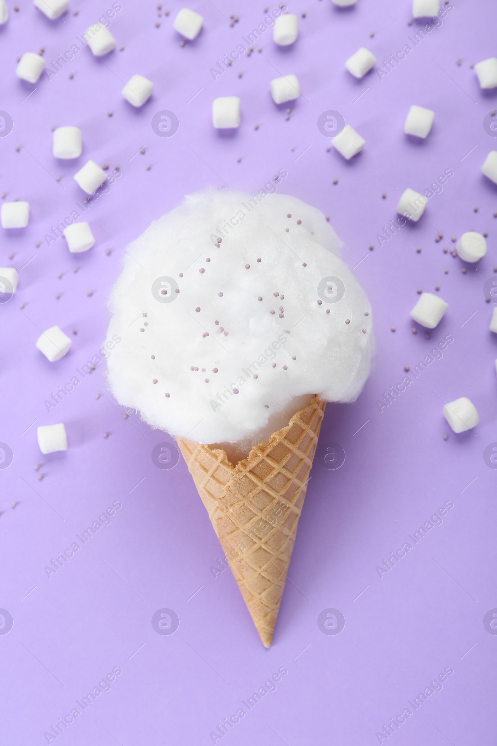 Photo of Sweet cotton candy in waffle cone and marshmallows on purple background, flat lay