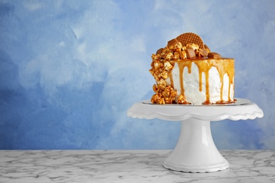 Dessert stand with delicious caramel cake on table against color background