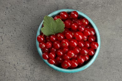 Photo of Ripe red currants and leaf in bowl on dark textured table, top view