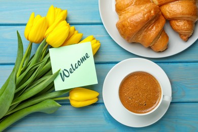 Image of Welcome card, beautiful yellow tulips, croissants and cup of aromatic coffee on light blue wooden table, flat lay