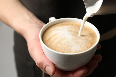 Photo of Woman pouring milk into cup of coffee on grey background, closeup