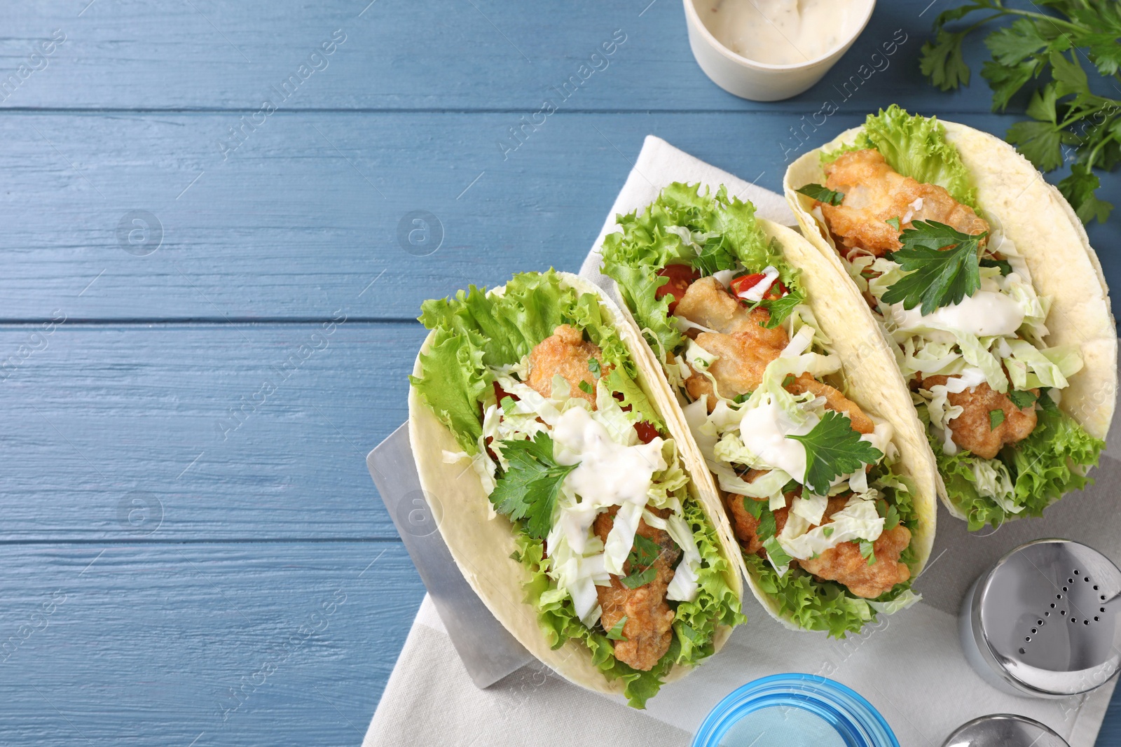 Photo of Yummy fish tacos served on blue wooden table, flat lay. Space for text
