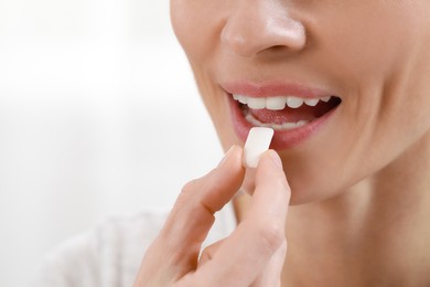 Photo of Woman putting chewing gum into mouth on blurred background, closeup