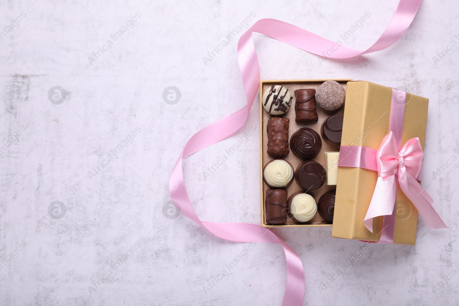 Open box with delicious chocolate candies and pink ribbon on white table, top view. Space for text Photo of Open box with delicious chocolate candies and pink ribbon on white table, top view. Space for text