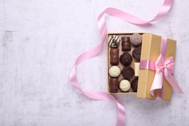 Photo of Open box with delicious chocolate candies and pink ribbon on white table, top view. Space for text