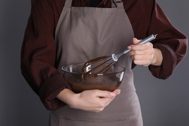 Woman with whisk making chocolate cream on grey background, closeup
