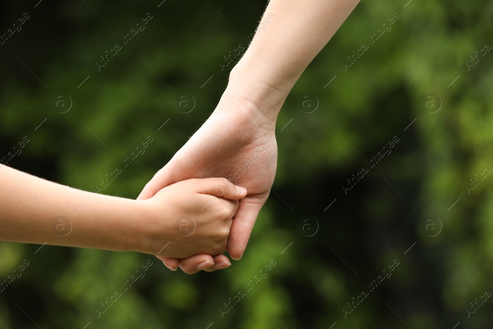 Photo of Woman and child holding hands outdoors, closeup
