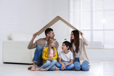 Happy family sitting under cardboard roof at home. Insurance concept