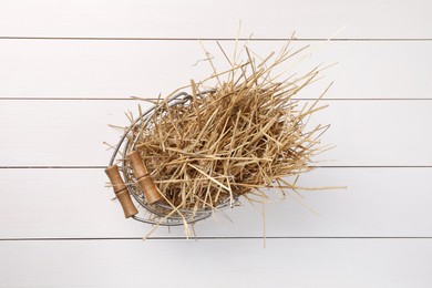 Photo of Dried straw in metal basket on white wooden table, top view
