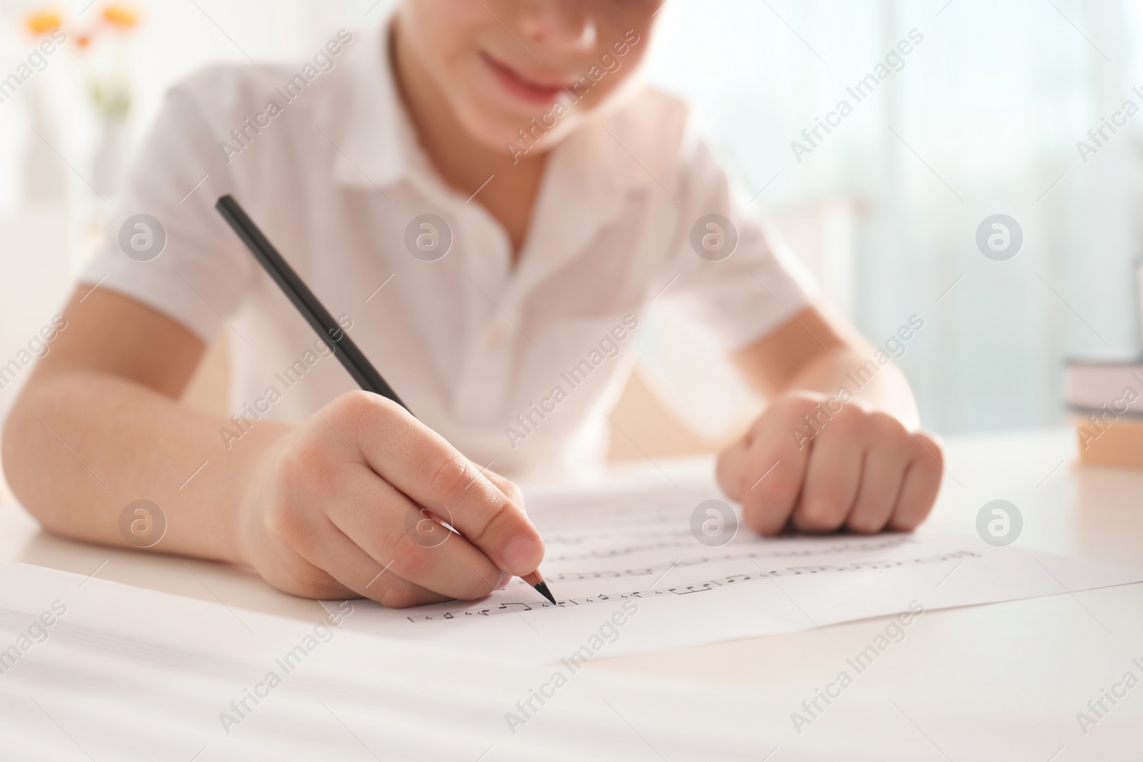 Photo of Little boy writing music notes at table, closeup
