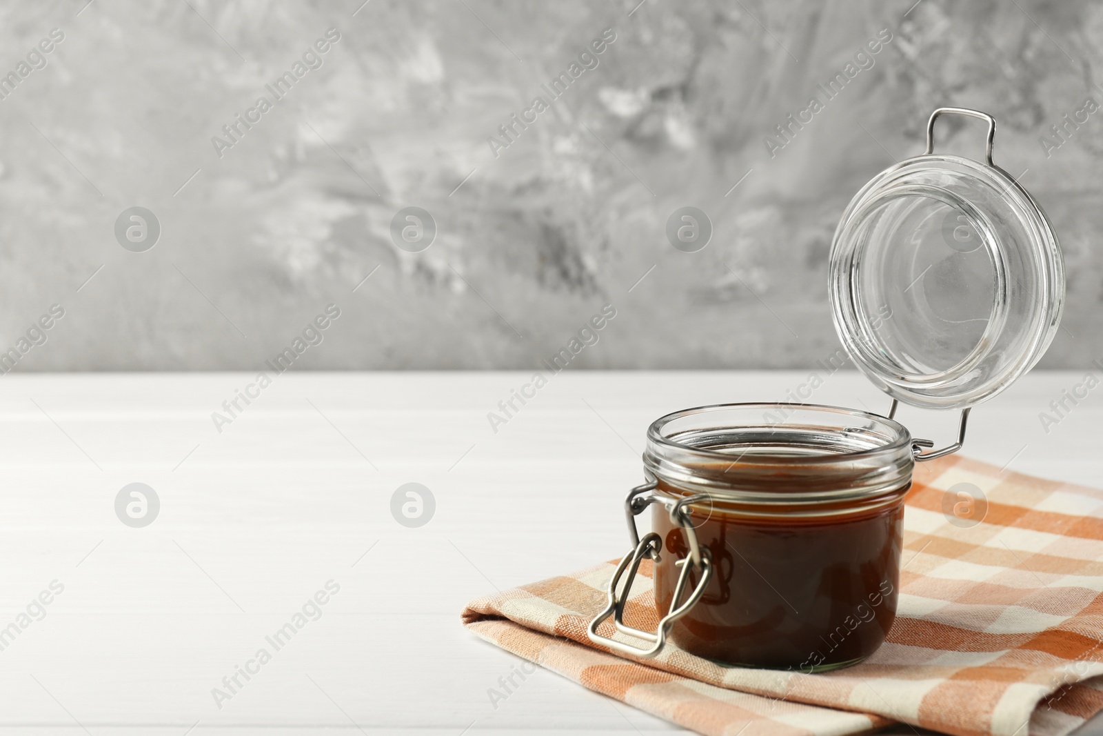 Photo of Tasty barbecue sauce in glass jar on white wooden table, space for text