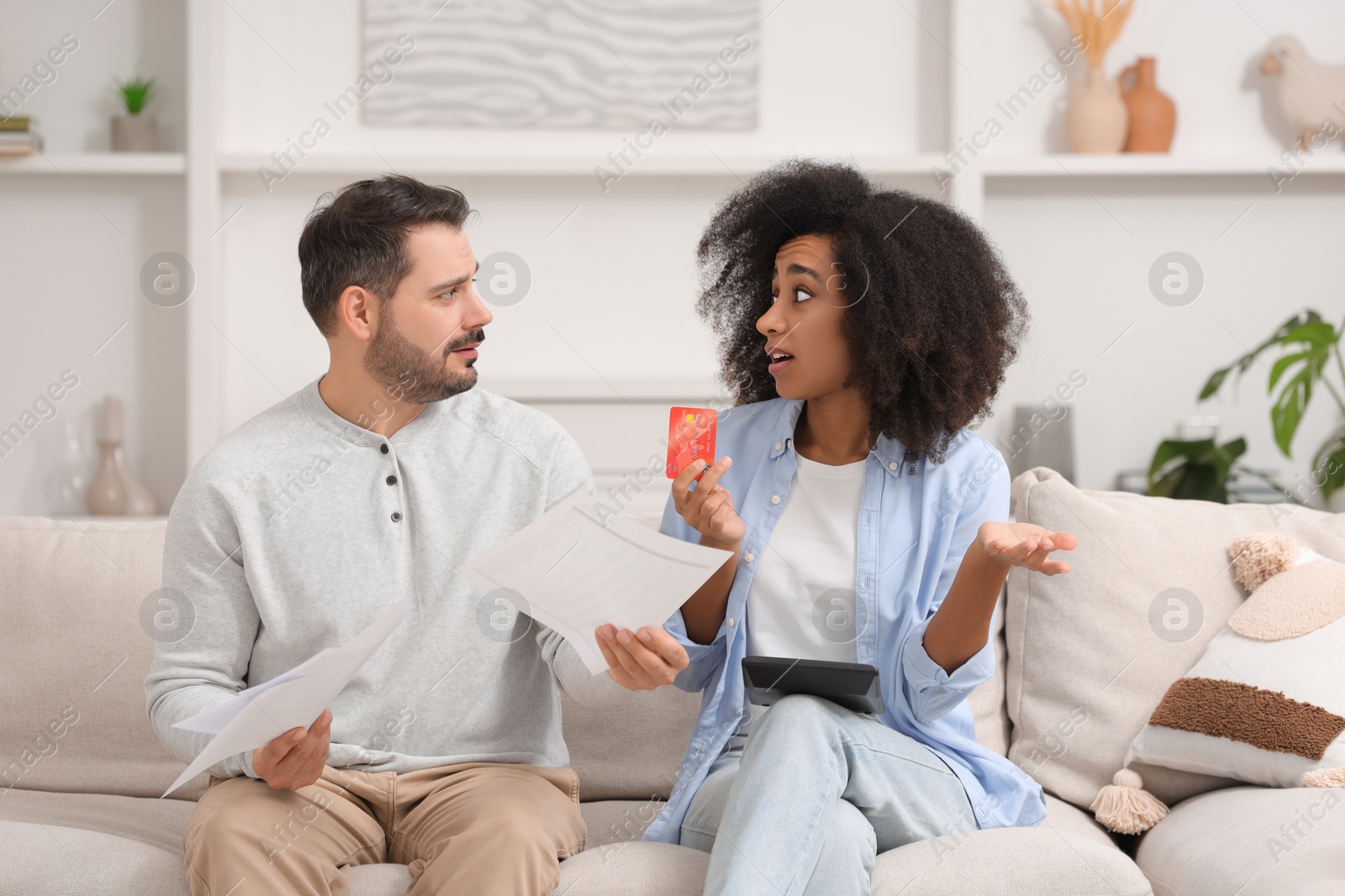 Photo of Shocked couple with debt notifications, calculator and credit card planning budget at home. Financial problem