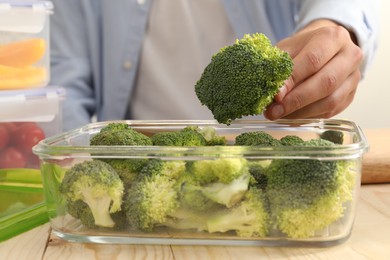 Photo of Man putting fresh broccoli into glass container at wooden table, closeup. Food storage
