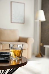 Glass of whiskey on wooden table in modern room interior, space for text