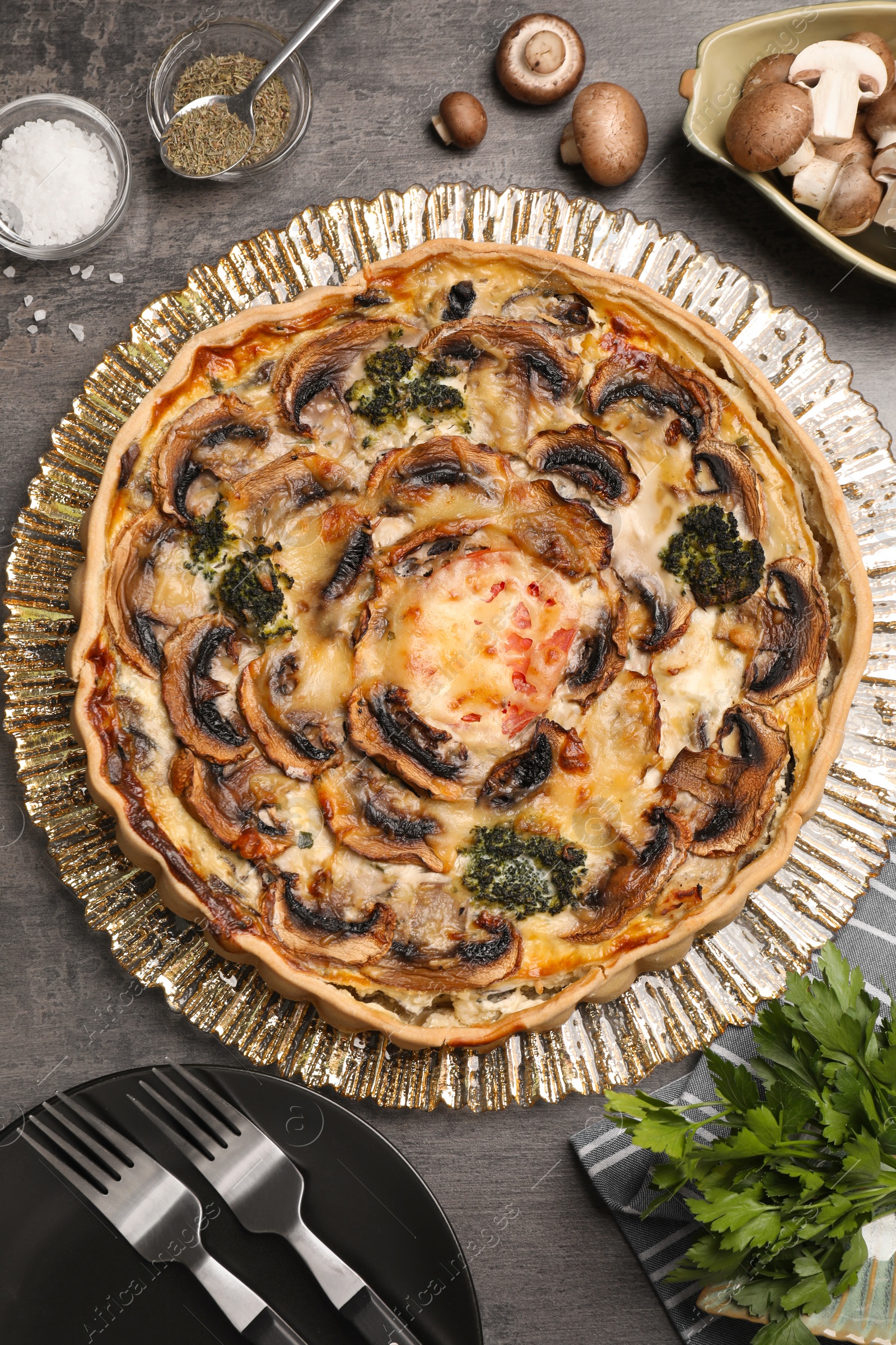Photo of Delicious quiche with mushrooms and ingredients on dark grey table, flat lay