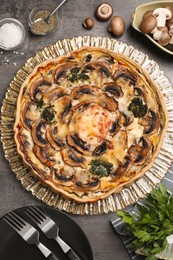 Photo of Delicious quiche with mushrooms and ingredients on dark grey table, flat lay