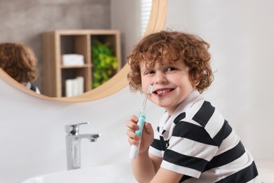 Cute little boy holding electric toothbrush in bathroom, space for text