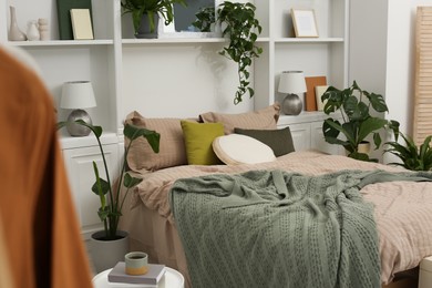 Comfortable bed and different houseplants in bedroom. Interior design