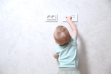 Photo of Little child playing with electrical socket indoors, back view. Dangerous situation