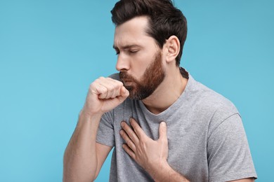 Sick man coughing on light blue background. Cold symptoms