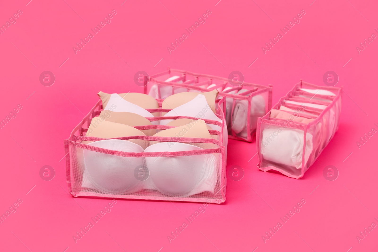 Photo of Transparent organizers with underwear on pink background