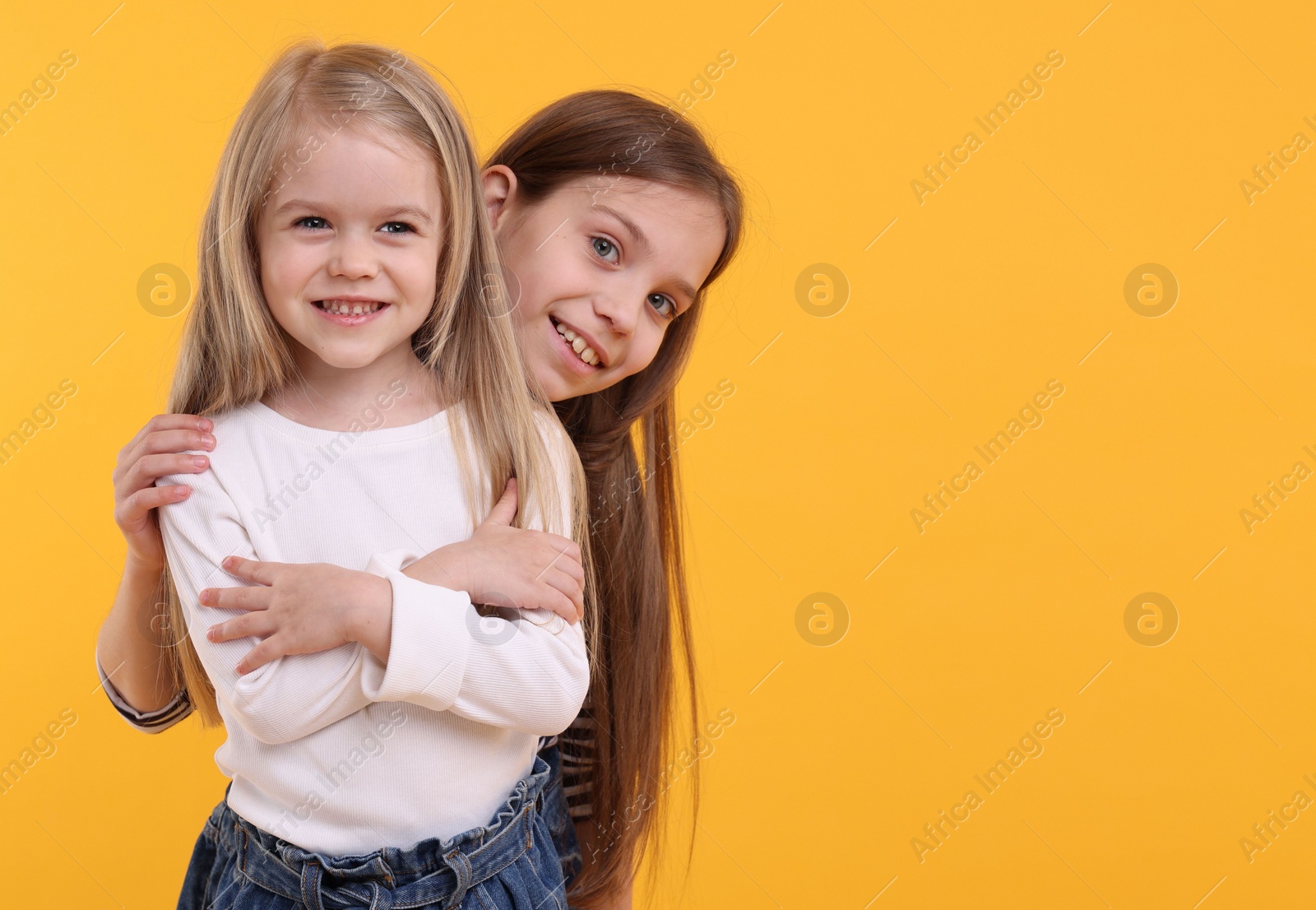 Photo of Portrait of cute little sisters on orange background, space for text