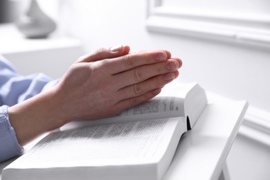 Religion. Christian woman praying over Bible indoors, closeup