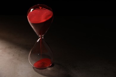 Photo of Hourglass with red flowing sand on grey table. Space for text