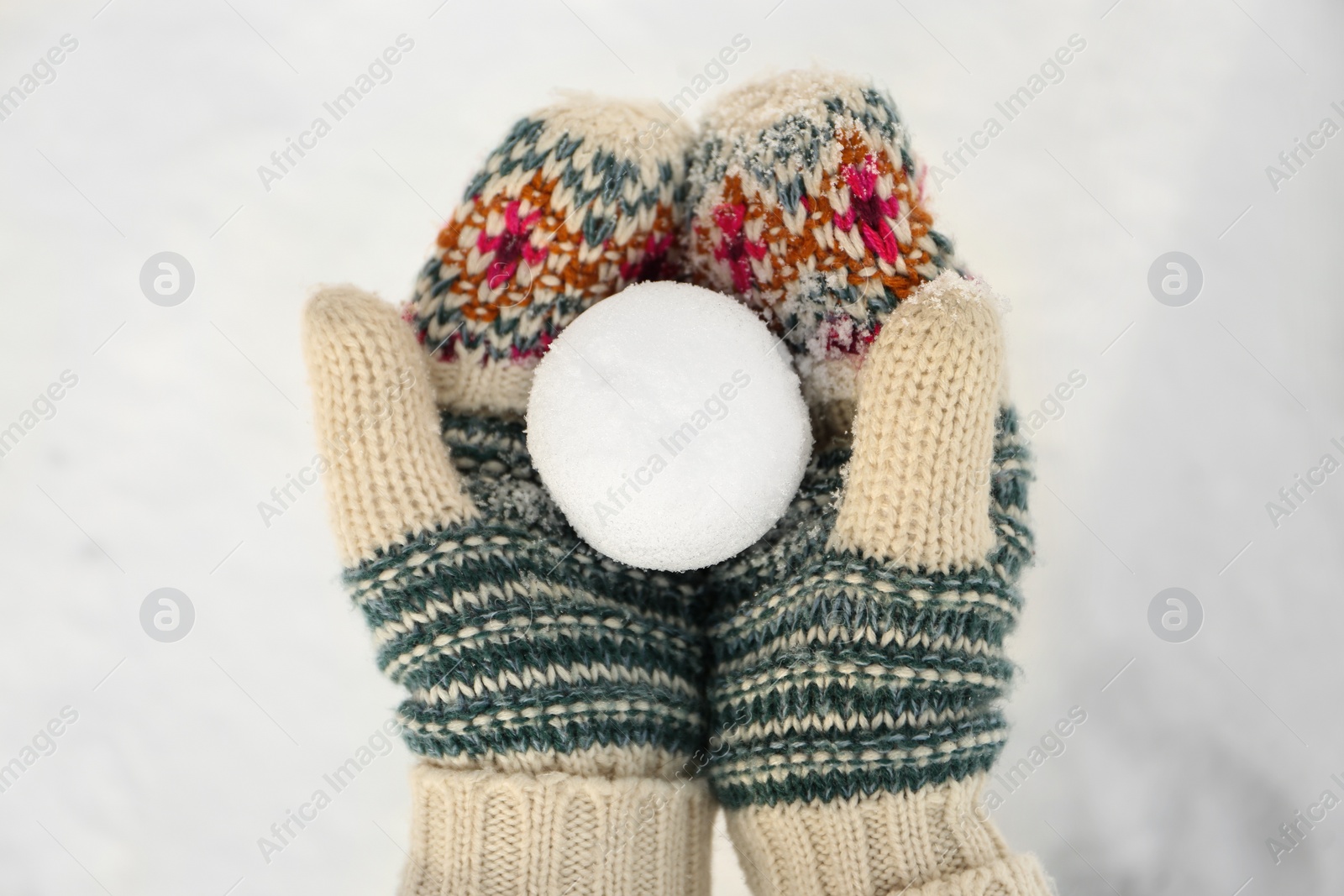 Photo of Woman in knitted mittens holding snowball outdoors, top view