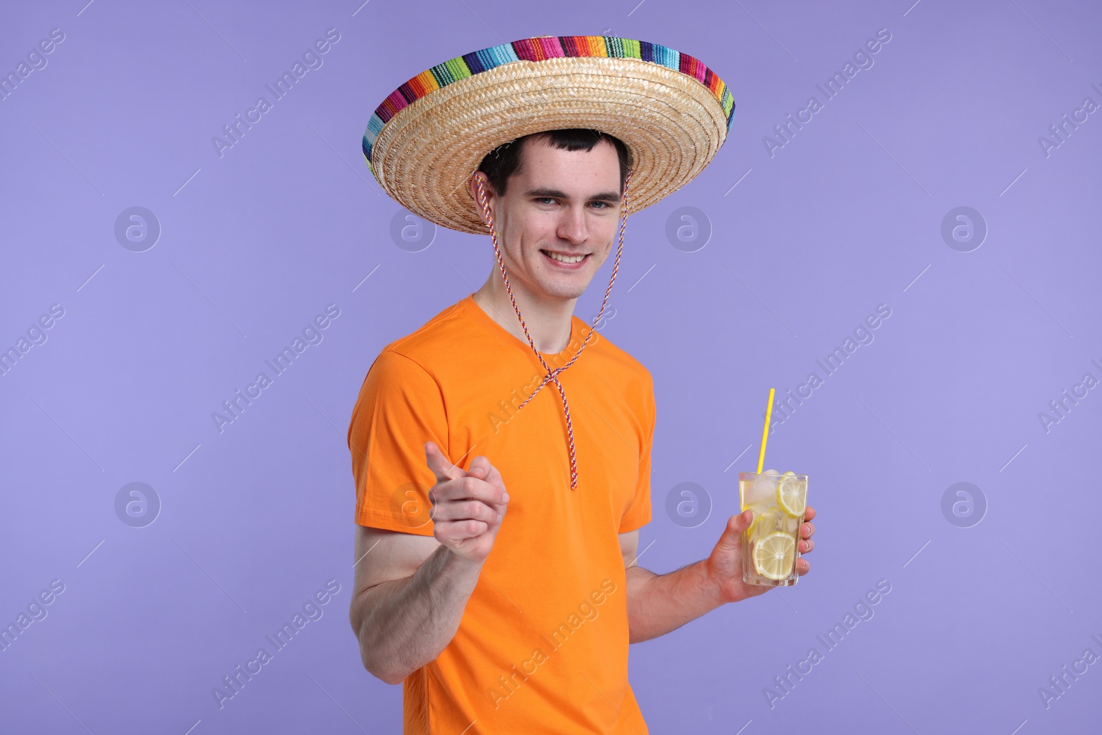 Photo of Young man in Mexican sombrero hat with cocktail on violet background