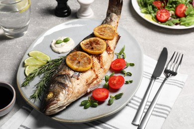 Photo of Delicious baked sea bass fish served with lemon, tomatoes and sauce on light grey table