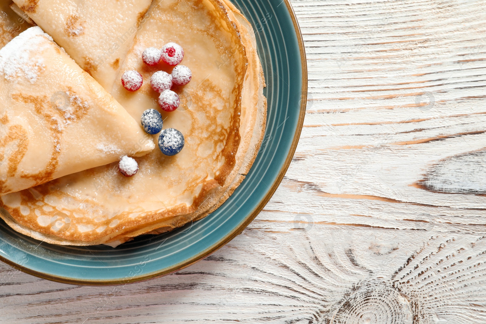 Photo of Thin pancakes served with sugar powder and berries on plate, top view