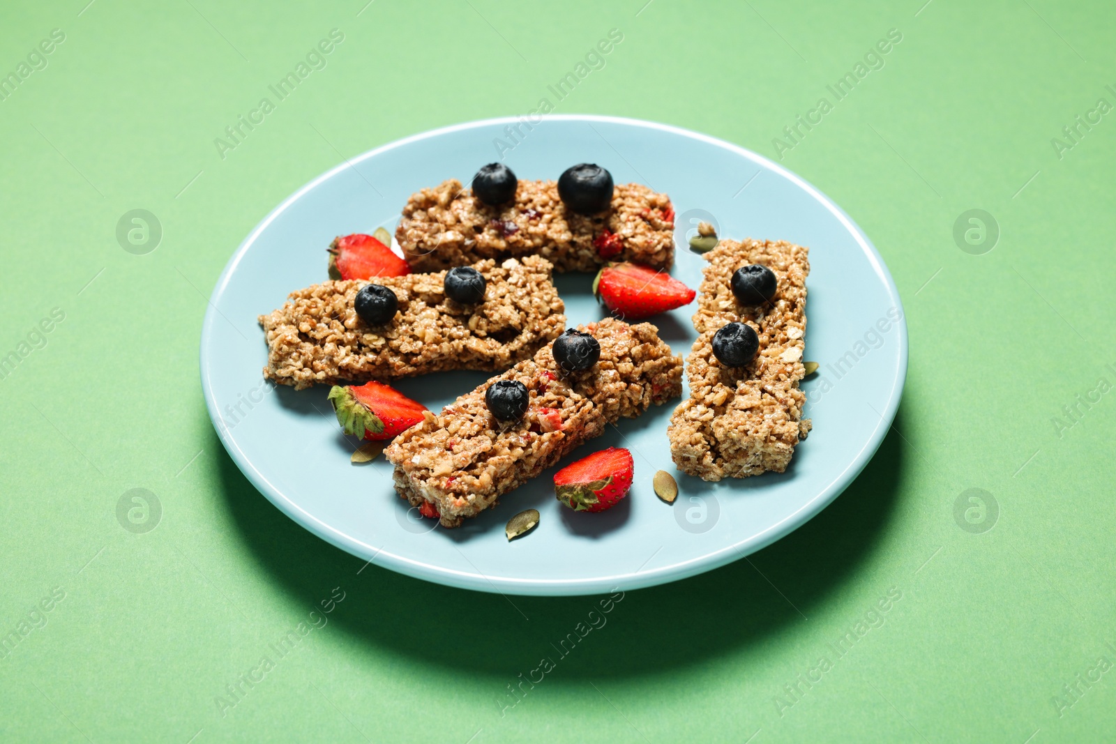 Photo of Tasty granola bars and berries on green table
