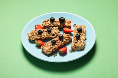 Tasty granola bars and berries on green table