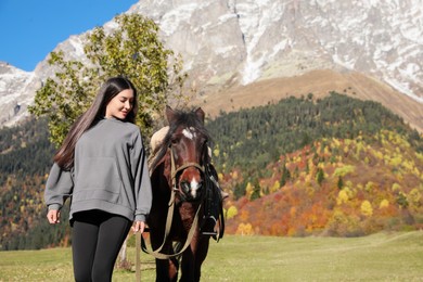 Photo of Young woman walking with horse in mountains on sunny day. Beautiful pet