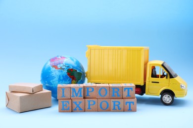 Photo of Words Import and Export made of wooden cubes, globe, boxes and toy truck on light blue background