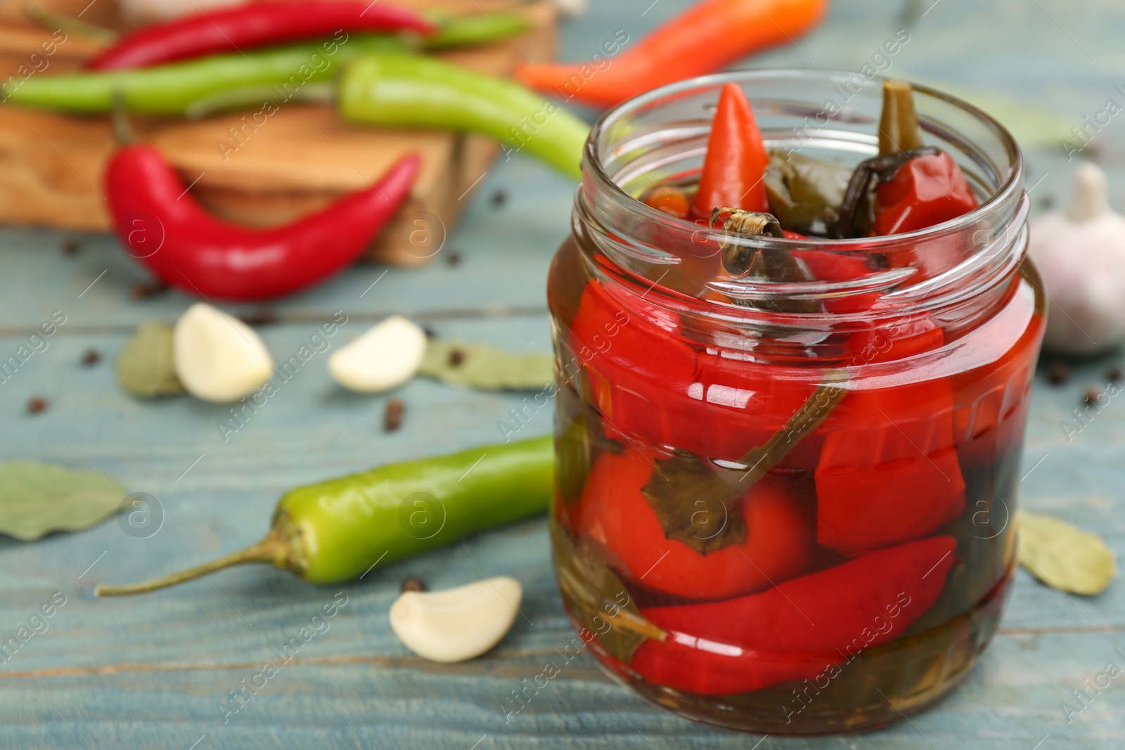 Photo of Glass jar of pickled chili peppers on light blue wooden table, closeup. Space for text