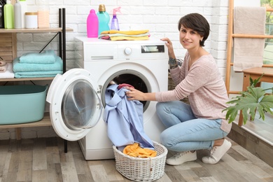 Photo of Young woman getting out clean clothes from washing machine at home