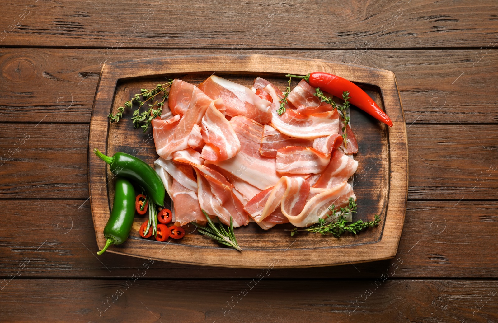 Photo of Board with raw bacon rashers on wooden background