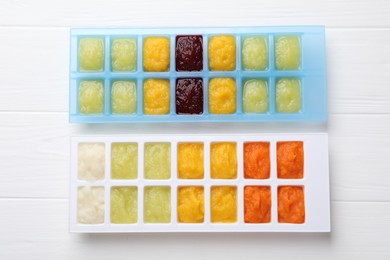 Photo of Different purees in ice cube trays on white wooden table, flat lay. Ready for freezing