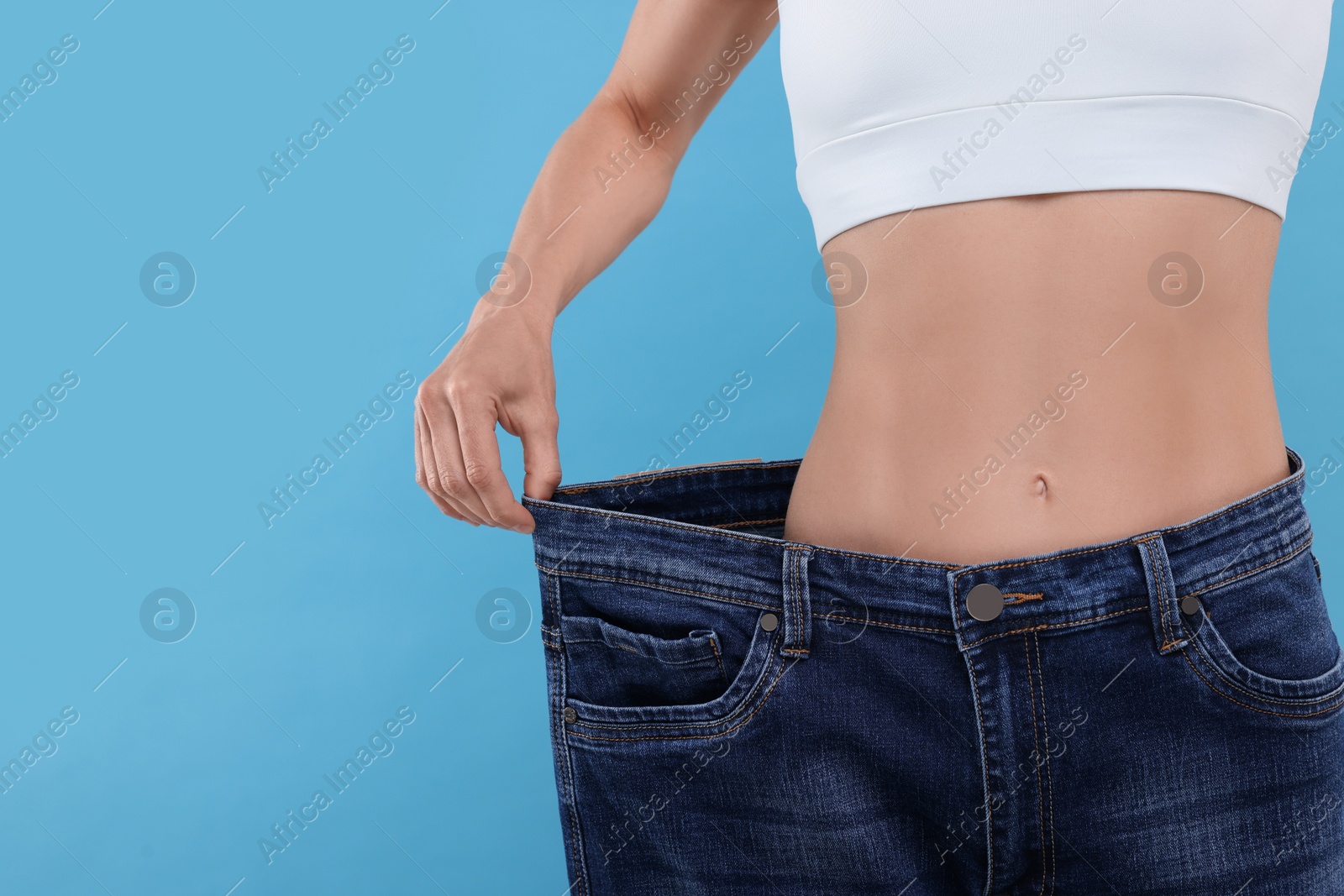 Photo of Slim woman wearing big jeans on light blue background, closeup and space for text. Weight loss